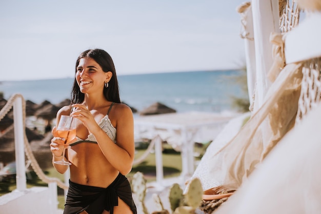 Mujer joven sonriente en bikini disfrutando de vacaciones en la playa mientras bebe cócteles