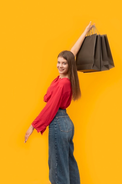 Mujer joven sonriente con bolsa de compras negra en sus manos sobre fondo amarillo Concepto de comprador Viernes negro Marco vertical