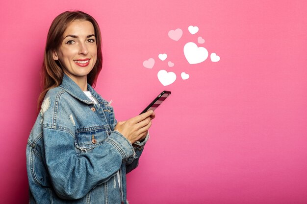 Mujer joven sonriente con bolsa ecológica mirando el teléfono en la pared rosa.