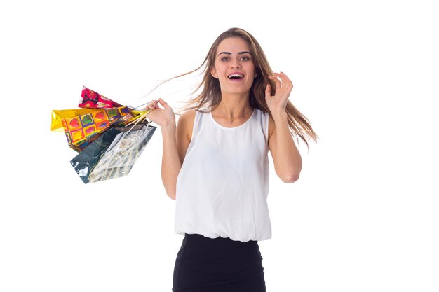 Mujer joven sonriente con cabello largo en blusa blanca y falda negra sosteniendo bolsas de compras en el estudio