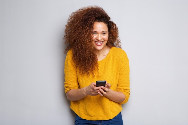 Mujer joven sonriente con el cabello rizado sosteniendo el teléfono celular