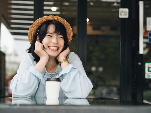 Mujer joven sonriente con café en la mesa sentada en una cafetería