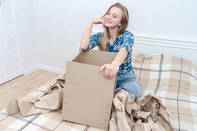Mujer joven sonriente con caja de cartón de desembalaje en la cama en casa Entrega de paquetes Orden en internet