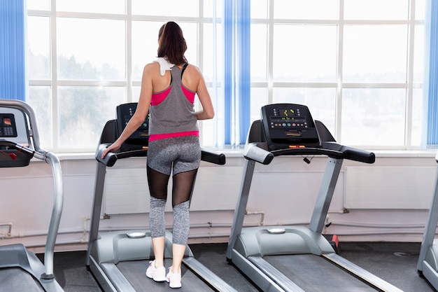 Mujer joven sonriente en una caminadora en el gimnasio. Estilo de vida activo y salud. Vista trasera.