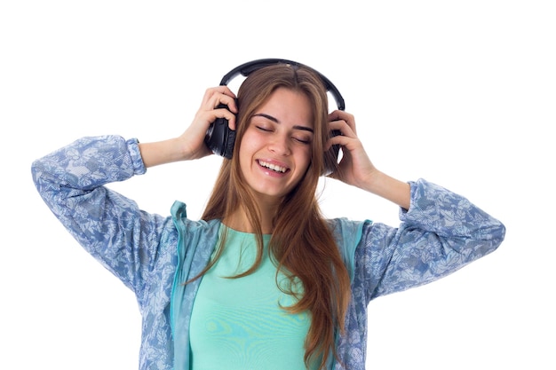 Mujer joven sonriente con camisa azul escuchando música con auriculares negros en el estudio