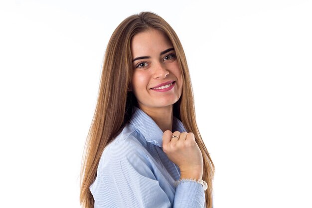 Mujer joven sonriente con camisa azul sosteniendo su cuello sobre fondo blanco en el estudio