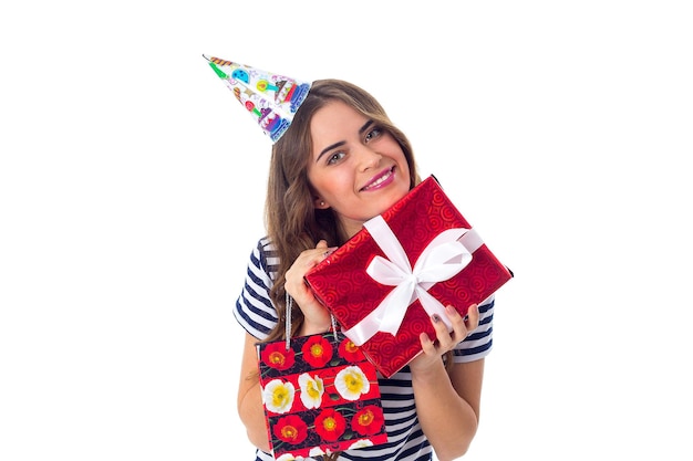 Mujer joven sonriente con camiseta despojada y gorra de celebración mostrando regalos de fondo blanco en el estudio