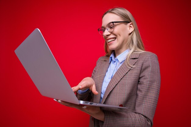 Una mujer joven sonriente con una computadora portátil sobre un fondo rojo Una mujer de negocios trabaja de forma remota