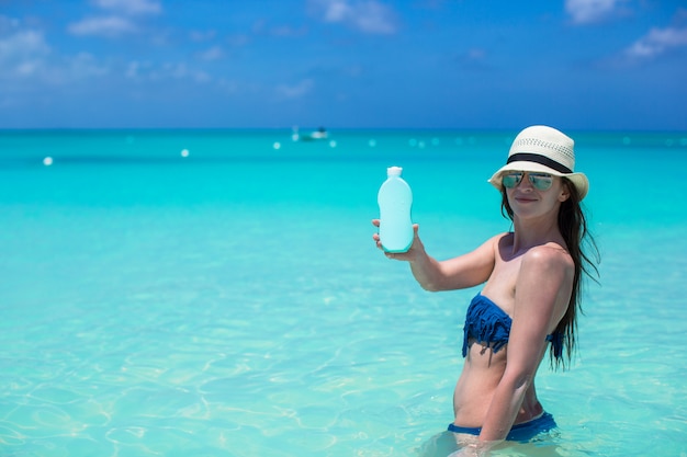 Mujer joven sonriente con crema solar en playa tropical