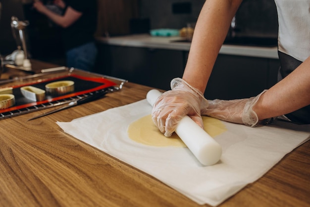 Mujer joven sonriente con delantal extendiendo masa con rodillo en las manos mujer feliz preparando desayuno panadero cocinando pastel o galletas en la cocina en casa de pie en la mesa