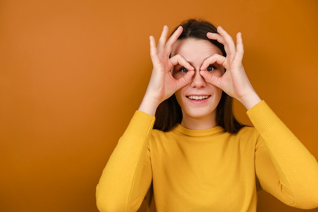 Mujer joven sonriente divertida que se divierte haciendo forma de gafas con las manos