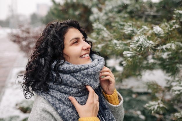 Foto mujer joven sonriente se encuentra en un parque de invierno cubierto de nieve helada.