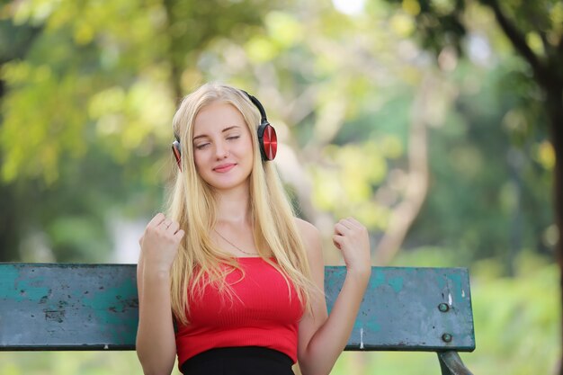 Mujer joven sonriente escuchando música sobre auriculares en el parque