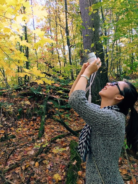 Mujer joven sonriente fotografiando contra los árboles en el bosque