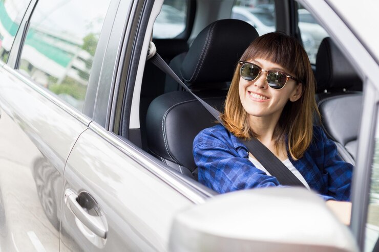 Mujer joven sonriente con gafas de sol manteniendo el volante en el coche vista delantera felicidad femenina asiática y disfrutando de la conducción sentada en el coche concepto de viaje concepto de seguro de seguridad primero