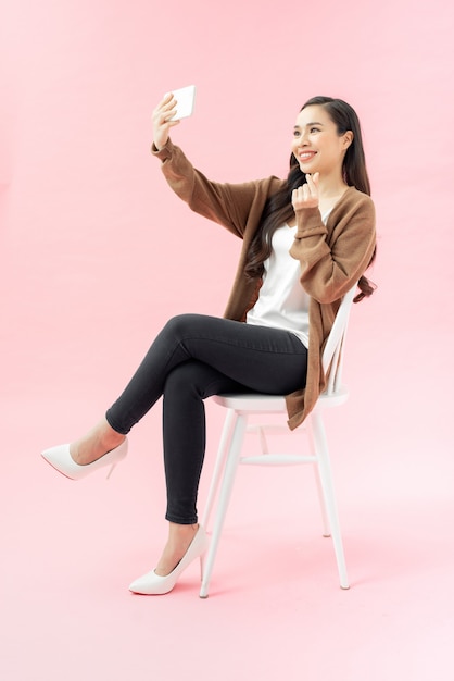 Mujer joven sonriente haciendo foto selfie en smartphone sobre fondo rosa