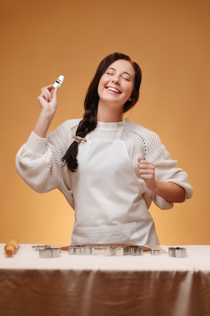 Mujer joven sonriente haciendo masa para hornear sobre fondo amarillo se prepara en delantal concepto de jengibre ...