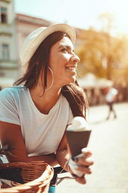 Mujer joven sonriente con helado, tomando un descanso en una plaza de la ciudad en un día soleado.