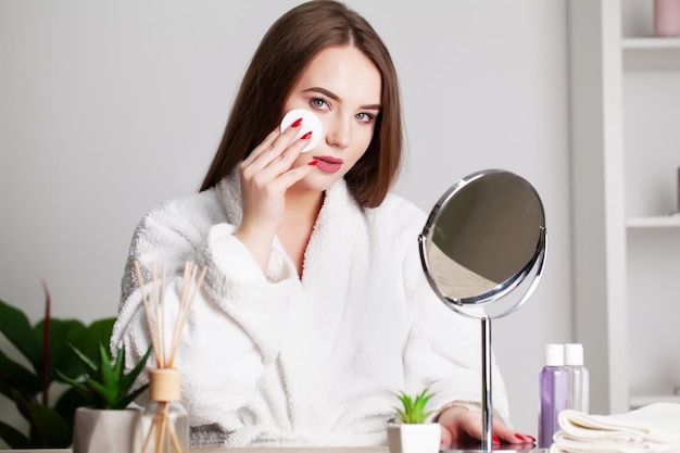 Mujer joven sonriente lavándose la cara con una esponja limpiadora facial en el baño.