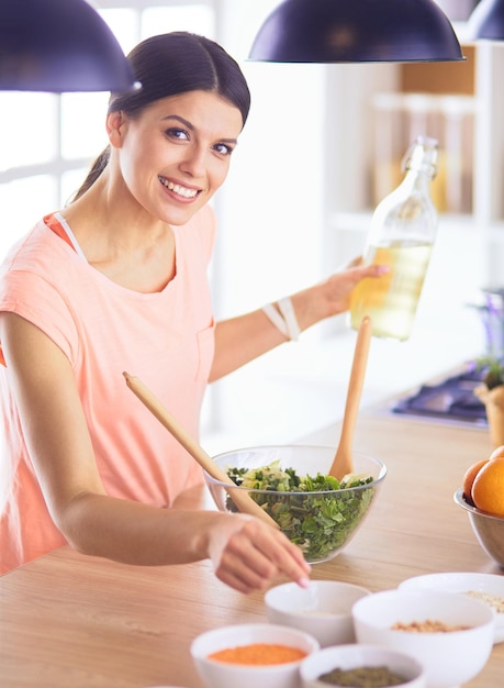 Mujer joven sonriente mezclando ensalada fresca en la cocina