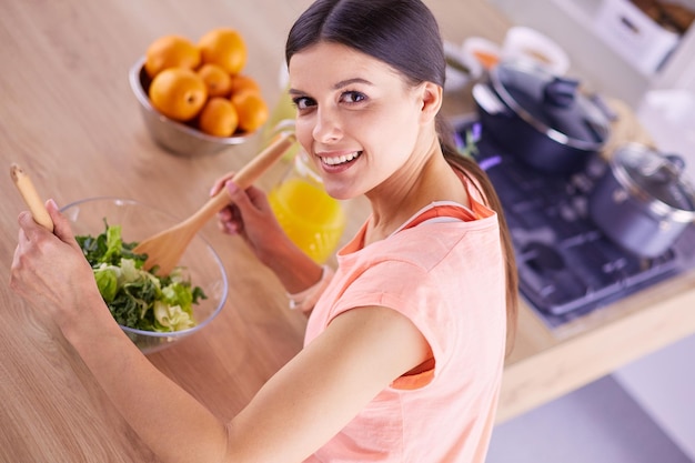 Mujer joven sonriente mezclando ensalada fresca en la cocina