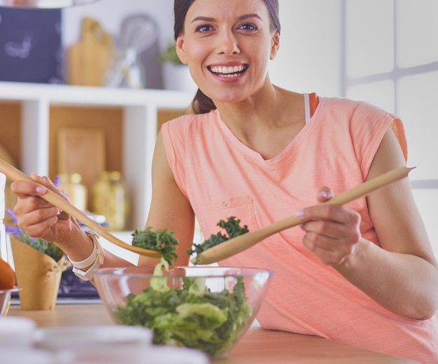 Mujer joven sonriente mezclando ensalada fresca en la cocina