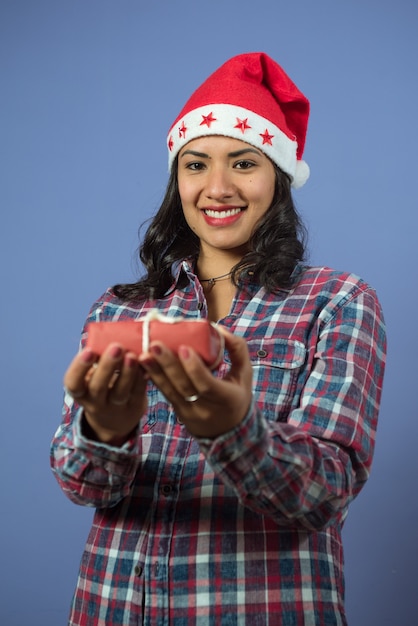 Mujer joven y sonriente mirando al frente tiene un pequeño regalo de Navidad