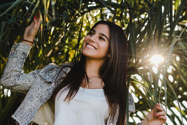 Foto mujer joven sonriente mirando hacia otro lado mientras está de pie contra las plantas