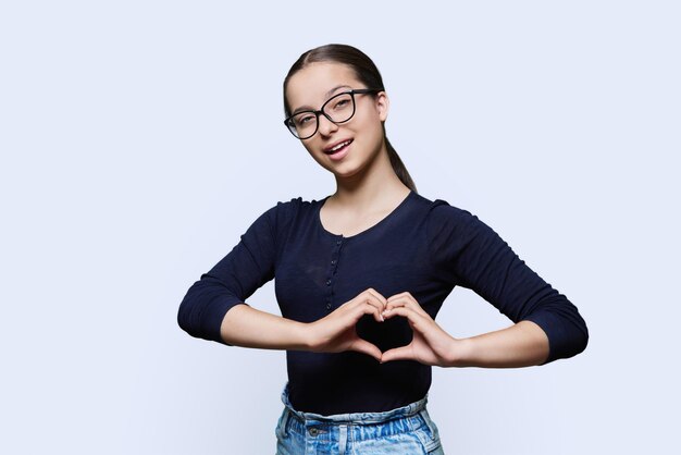 Mujer joven sonriente mostrando gesto de corazón con los dedos fondo blanco