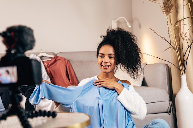 Foto mujer joven sonriente mostrando el vestido mientras filma en casa