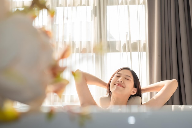 Mujer joven sonriente con los ojos cerrados sentada en la bañera