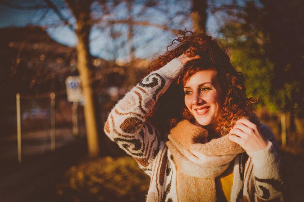 Foto una mujer joven sonriente de pie contra los árboles durante un día soleado