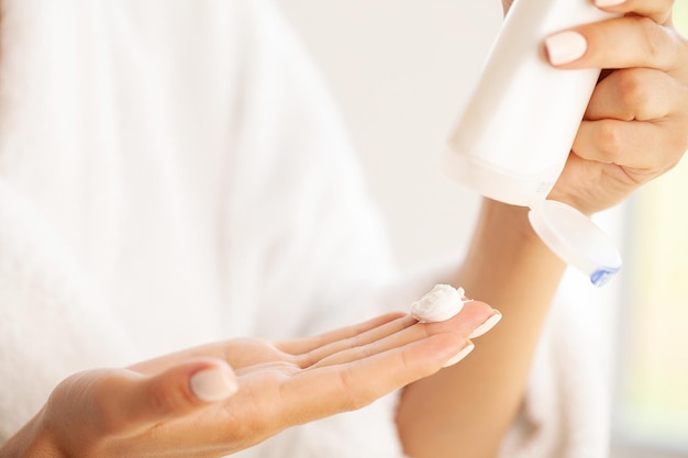 Mujer joven sonriente que aplica la crema de cara de la humedad