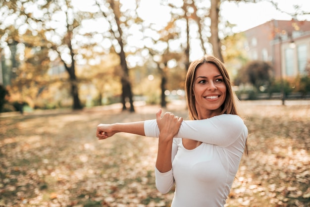 La mujer joven sonriente que hace estiramiento ejercita en el parque.