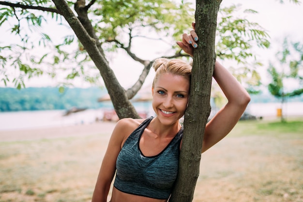 Mujer joven sonriente que se inclina en un árbol en la playa. De cerca.