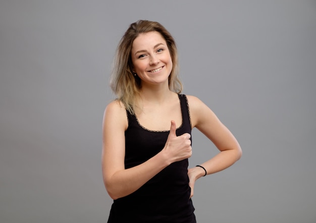 Mujer joven sonriente que muestra los pulgares arriba gesto