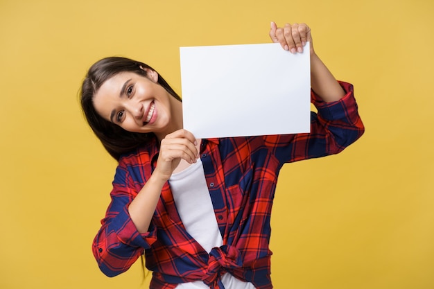 Mujer joven sonriente que sostiene la hoja de papel blanco. Retrato de estudio sobre fondo amarillo.