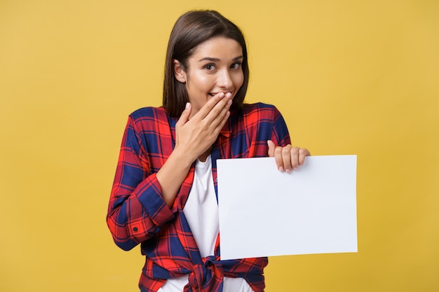 Mujer joven sonriente que sostiene la hoja de papel blanco. Retrato de estudio sobre fondo amarillo.