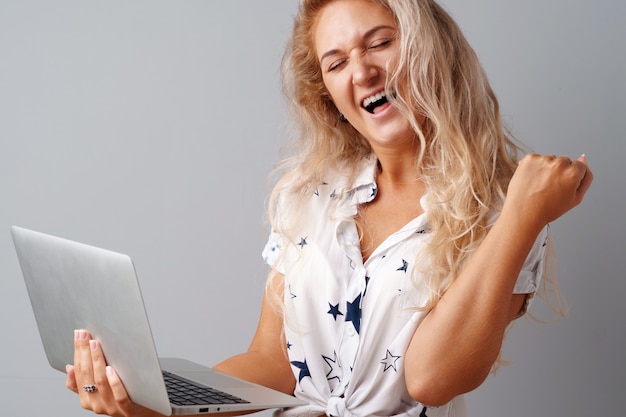 Mujer joven sonriente que sostiene el ordenador portátil sobre fondo gris