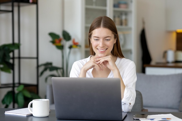 Foto mujer joven sonriente que trabaja en la computadora portátil en la oficina en casa. concepto de formación virtual o estudio remoto