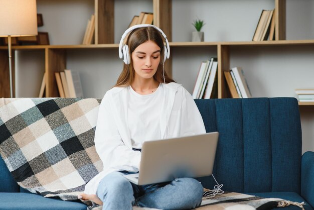 Mujer joven sonriente que usa una computadora portátil sentada en el sofá en casa hermosa chica comprando o chateando en línea en las redes sociales divirtiéndose viendo películas freelance trabajando en un proyecto de computadora