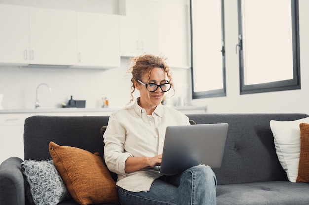 Mujer joven sonriente que usa una computadora portátil sentada en el sofá en casa hermosa chica comprando o chateando en línea en las redes sociales divirtiéndose viendo películas freelance trabajando en un proyecto de computadoraxA