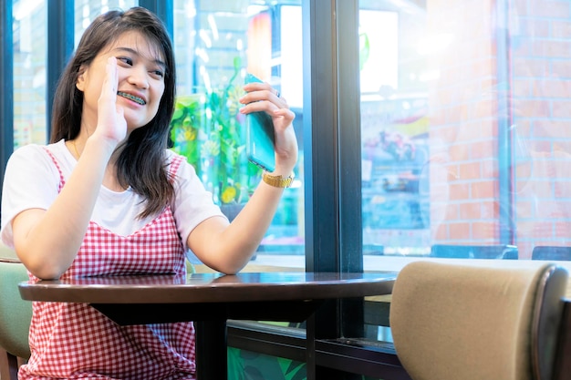 Mujer joven sonriente que usa Smartphone y hace videollamadas en el café Agita tus manos Diviértete mientras usas xAI Es muy popular en el presente