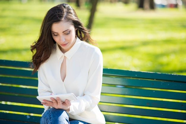 Mujer joven sonriente que usa su tableta en un parque