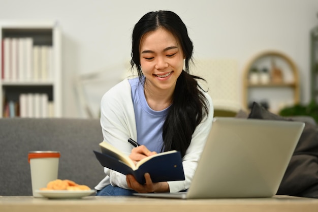 Mujer joven sonriente con ropa informal usando una computadora portátil en el sofá en casa Tecnología y estilo de vida de la gente