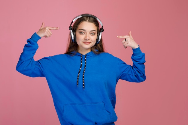 Mujer joven sonriente señalando auriculares plateados mientras escucha música