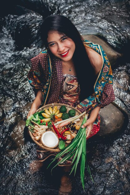 Foto mujer joven sonriente sentada con comida en la orilla del río en el bosque