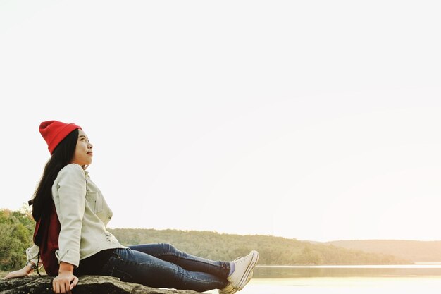 Foto mujer joven sonriente sentada junto al lago contra un cielo despejado