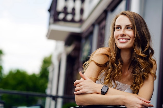 Mujer joven sonriente con smartwatches relajarse y sentarse en una silla al aire libre