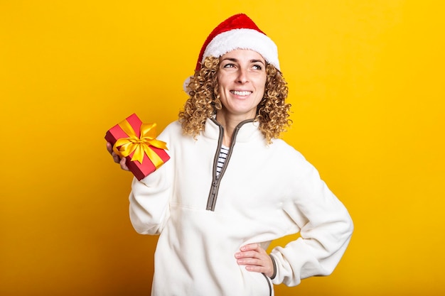 Mujer joven sonriente con sombrero de santa claus con caja de regalo sobre fondo amarillo